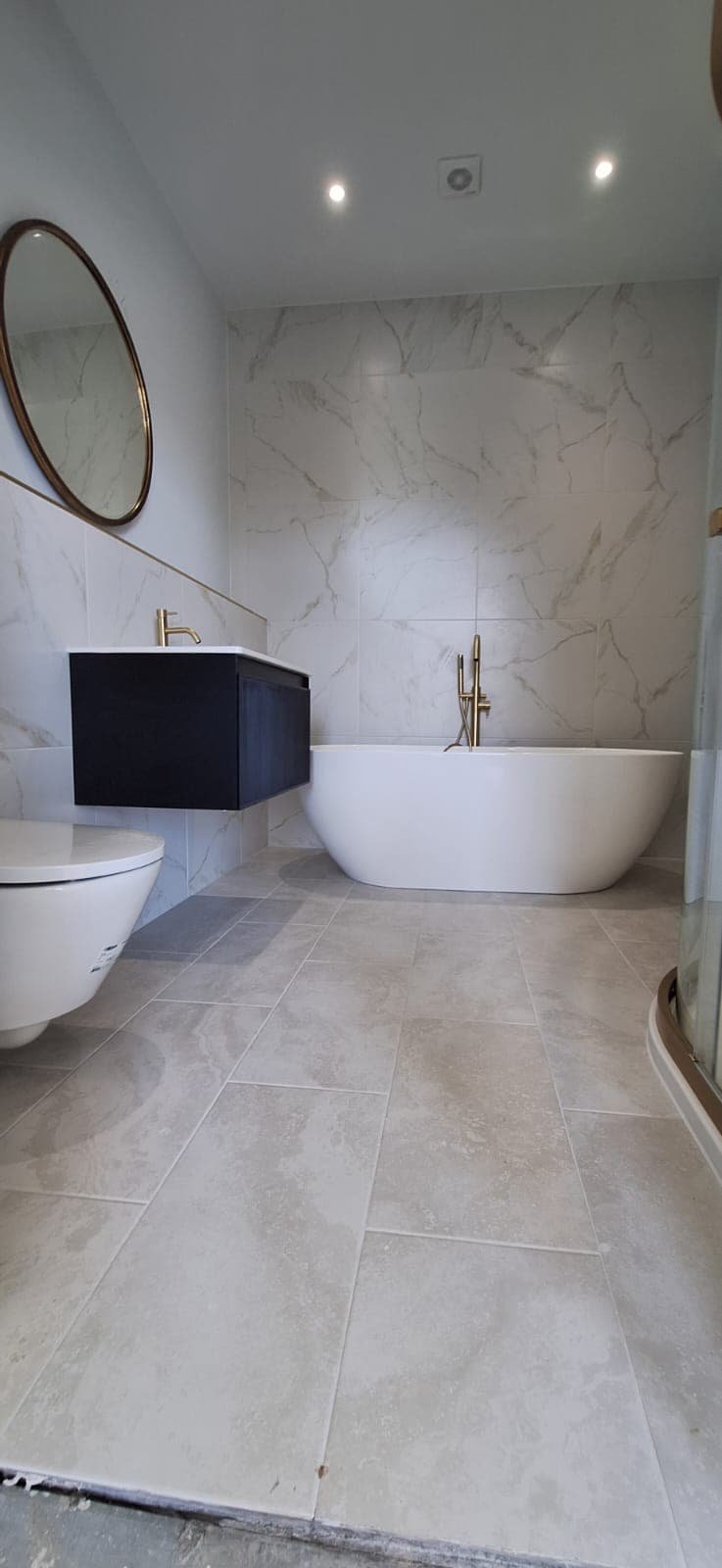 A finished marble bathroom with a freestanding bath and gold taps